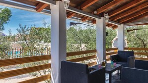 An outdoor patio with wicker furniture and a view of a pool and trees.