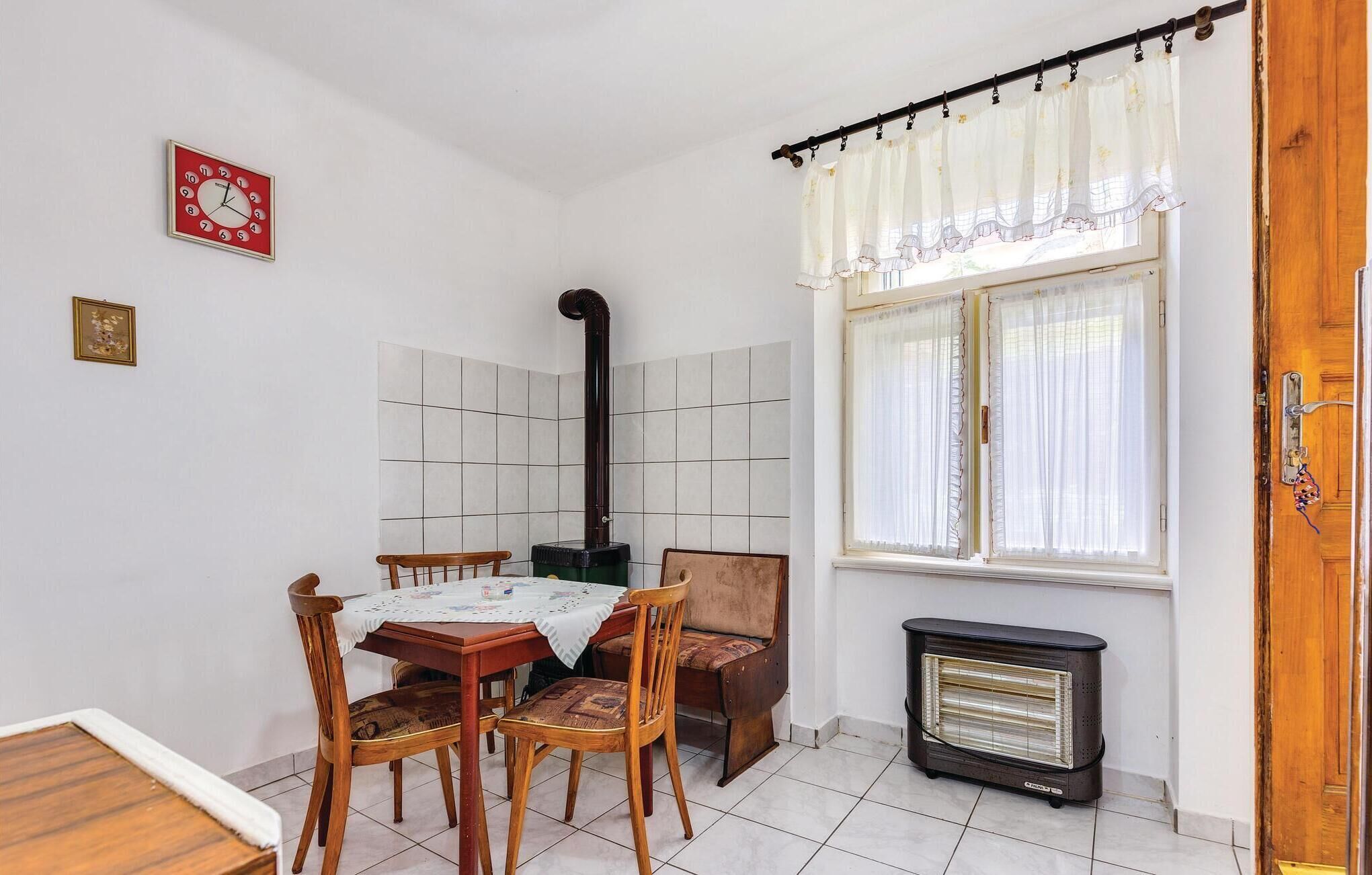 A room with a tiled floor, a table with chairs, a heater, and a window with curtains.