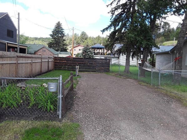A gravel driveway leading to a fenced property with a wooden fence, a metal gate, and a small shed. - Rail house 3 bedroom, 2 bath, 2 story house. Lots parking Downtown Hill City, SD (Hill City)