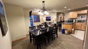 A dining area with a dark wooden table and chairs, a chandelier, and a view of the outside through a window.