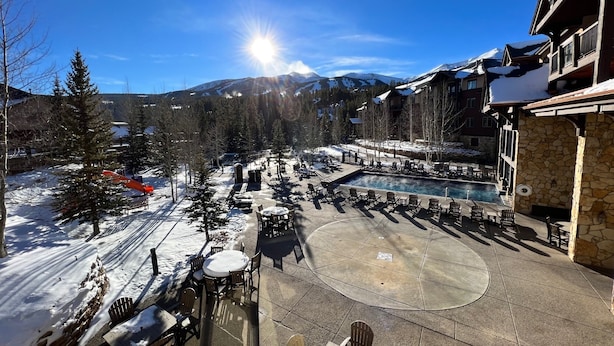 A resort with outdoor seating and a pool, surrounded by snow-covered mountains and trees.