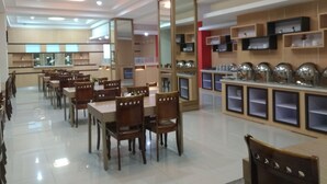 A spacious restaurant with multiple dining tables and chairs, a kitchen area with shelves, and a bright interior. - Hotel Rangkayo Basa Padang Panjang (Padang Panjang)