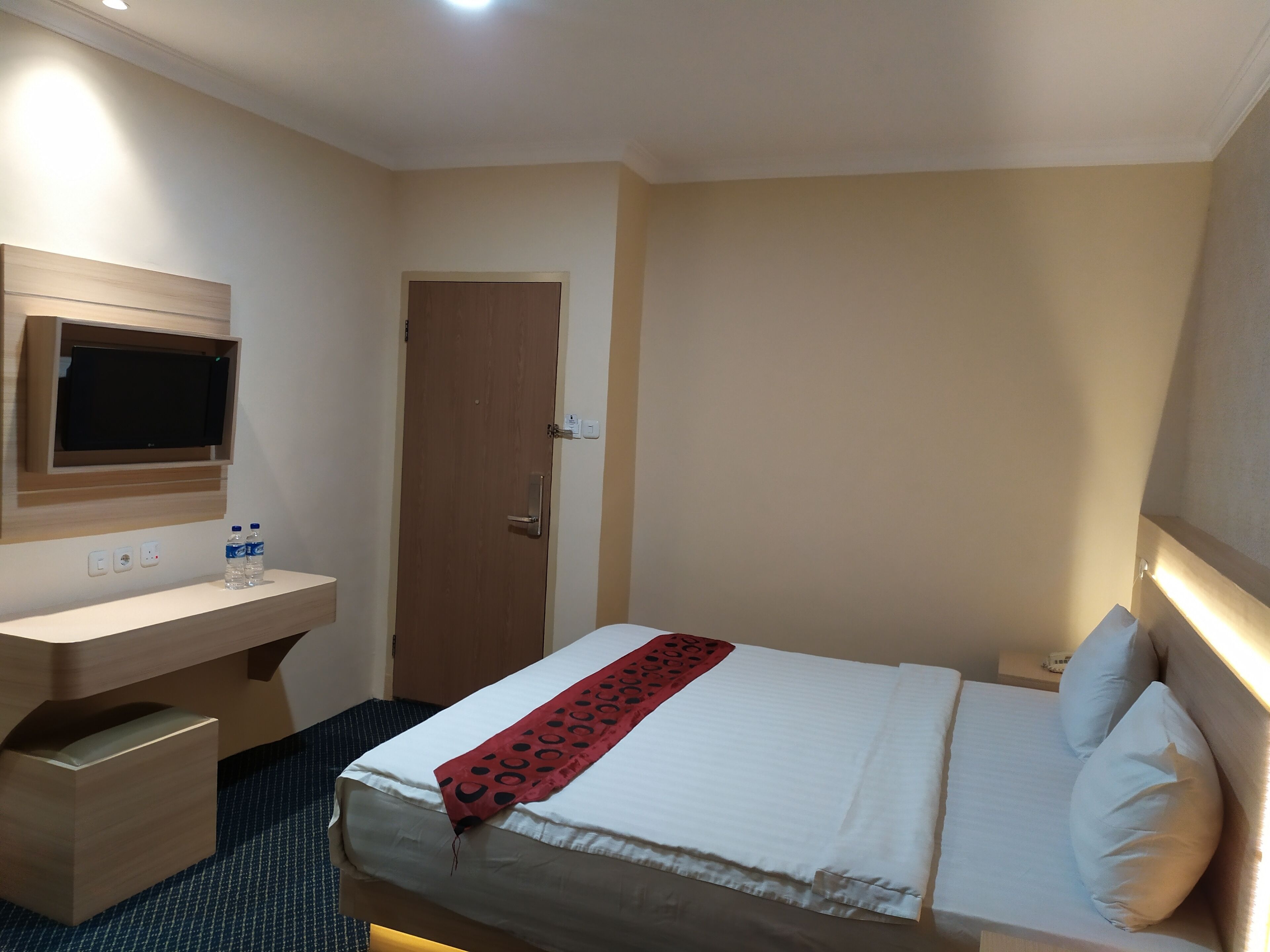 A hotel room with a bed, bedside table, TV, and a door.