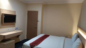 A hotel room with a bed, bedside table, TV, and a door.