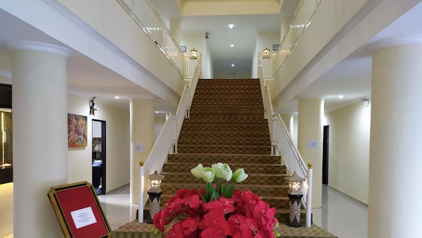 A hotel lobby with a grand staircase, a reception desk, and a floral arrangement. - Hotel Rangkayo Basa Padang Panjang (Padang Panjang)