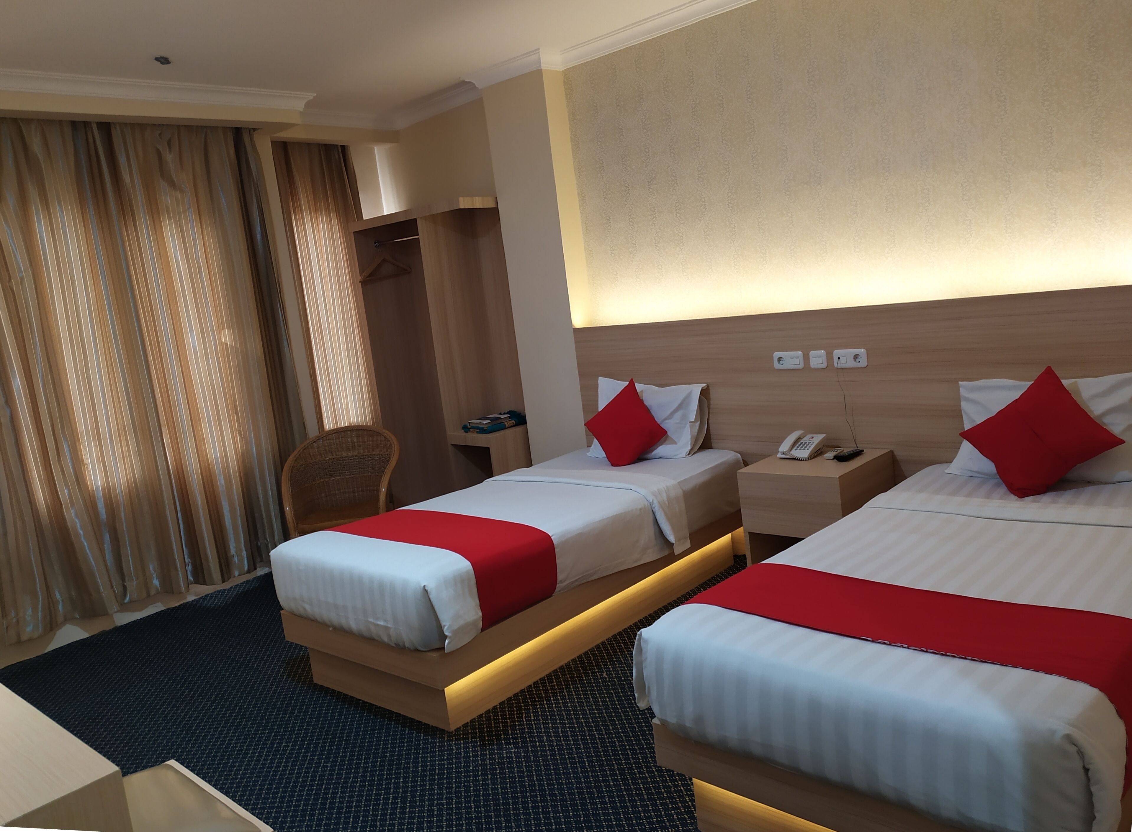 A hotel room with two beds, a desk, a chair, and a wardrobe.