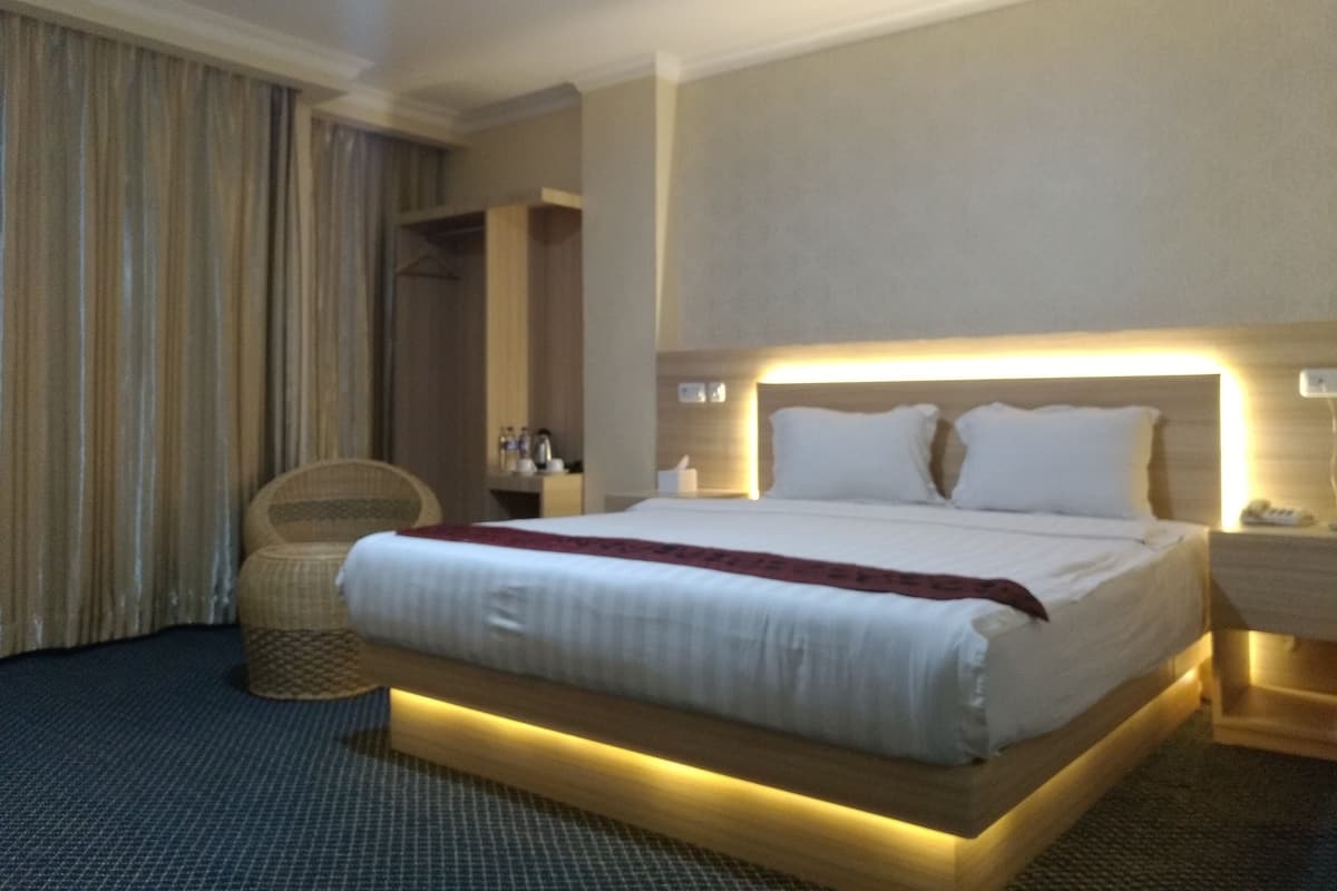 Una habitación de hotel con una cama grande, mesitas de noche, una silla y un armario.