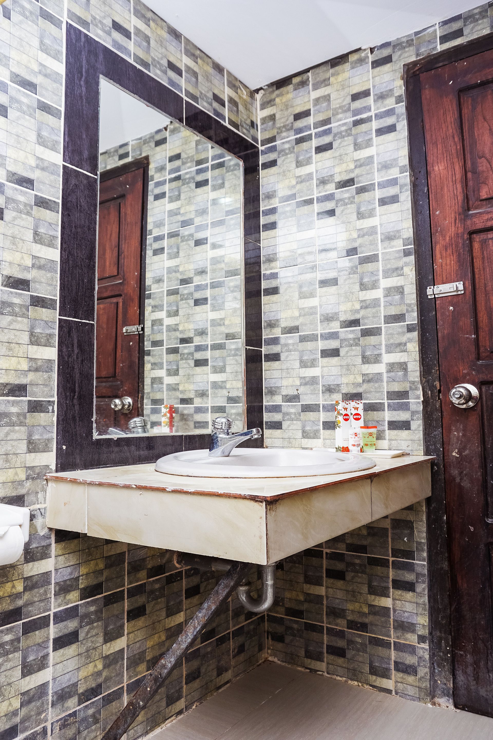 Une salle de bain avec un mur carrelé, un lavabo, un miroir et une porte en bois.