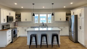 A spacious kitchen with white cabinets, a large island with stools, stainless steel appliances, and pendant lighting. - Your Home Away From Home- 4 bed, 3 bath, centrally located. (Mermaid)