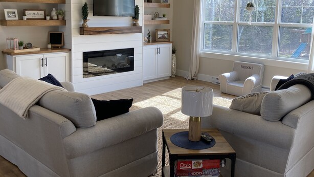 A modern living room with a fireplace, built-in TV, and a large window with a view of the outdoors. - Your Home Away From Home- 4 bed, 3 bath, centrally located. (Mermaid)
