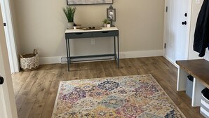 A hallway with a wooden floor, a patterned rug, a console table with decorative items, and a door with a coat rack. - Your Home Away From Home- 4 bed, 3 bath, centrally located. (Mermaid)