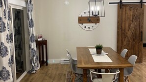 A dining area with a wooden table, white chairs, a hanging light fixture, and a rustic barn door. - Your Home Away From Home- 4 bed, 3 bath, centrally located. (Mermaid)