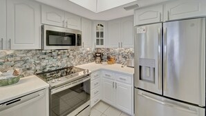 A modern kitchen with white cabinetry, a stainless steel refrigerator, a microwave, and a tiled backsplash. - Very Nice and Comfortable with a Great View of the Gulf on the Resort, A3724A (Cape Haze)