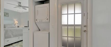 A compact bedroom with a bed, a ceiling fan, a washing machine, and a frosted glass door with a "No Smoking" sign.