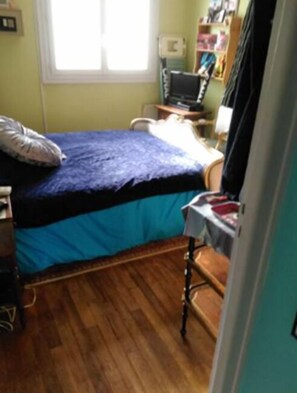 A bedroom with a bed, a desk with a computer, and a window.