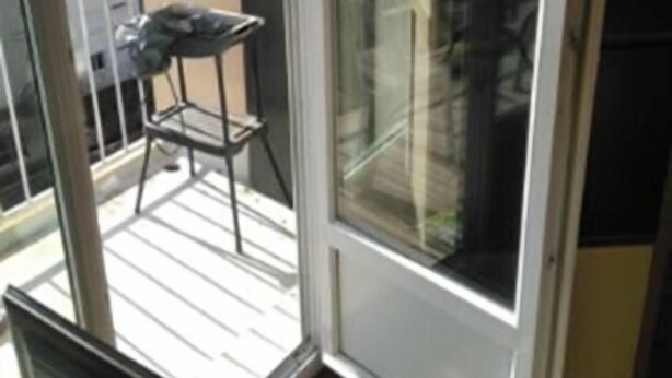 A balcony with a chair and a small table, a sliding glass door, and a view of a building outside.
