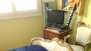 A bedroom with a bed, a chair, a television, and a guitar.