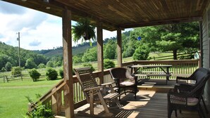 Une terrasse en bois, meublée de meubles en osier, avec vue sur un paysage verdoyant.