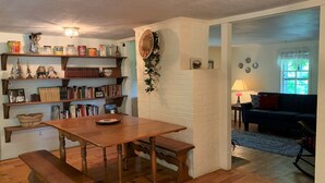 Un salon chaleureux avec une table à manger en bois, des bancs et des étagères remplies de livres et d’objets décoratifs.