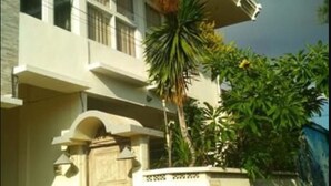 A two-story building with a balcony, a gated entrance, and a small garden with palm trees. - Kunigen Villa Kuta Bali (Kerobokan)
