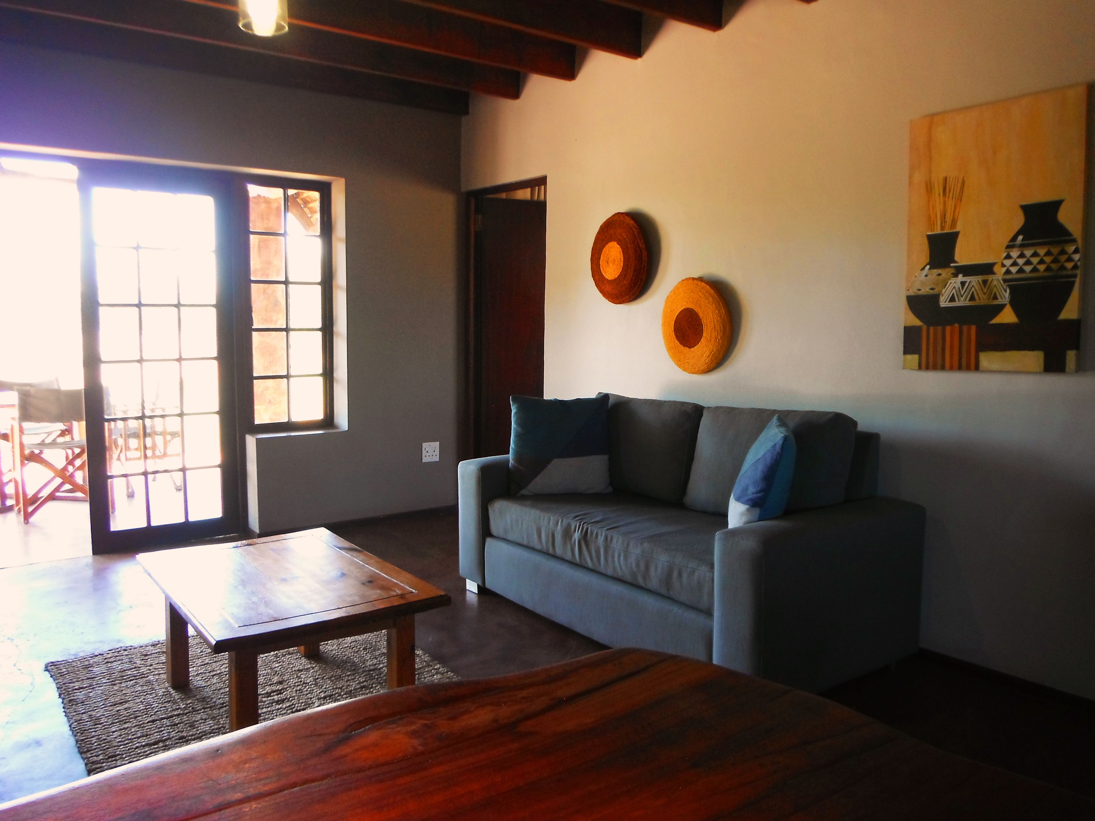 A living room with a sofa, a coffee table, and a wooden bench. There is a large window with blinds, a door, and a wall with decorative plates.
