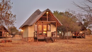Een landelijke lodge met rieten dak, houten gevel en een veranda met zitplaatsen.