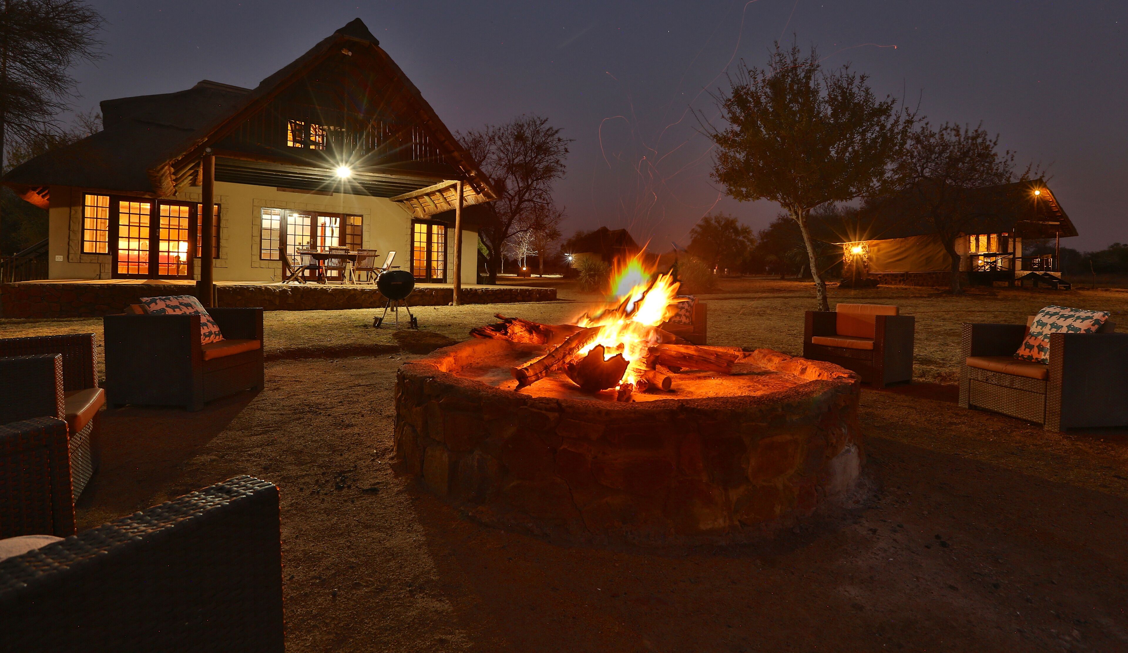 A rustic lodge with a stone fire pit in the foreground, surrounded by outdoor seating.