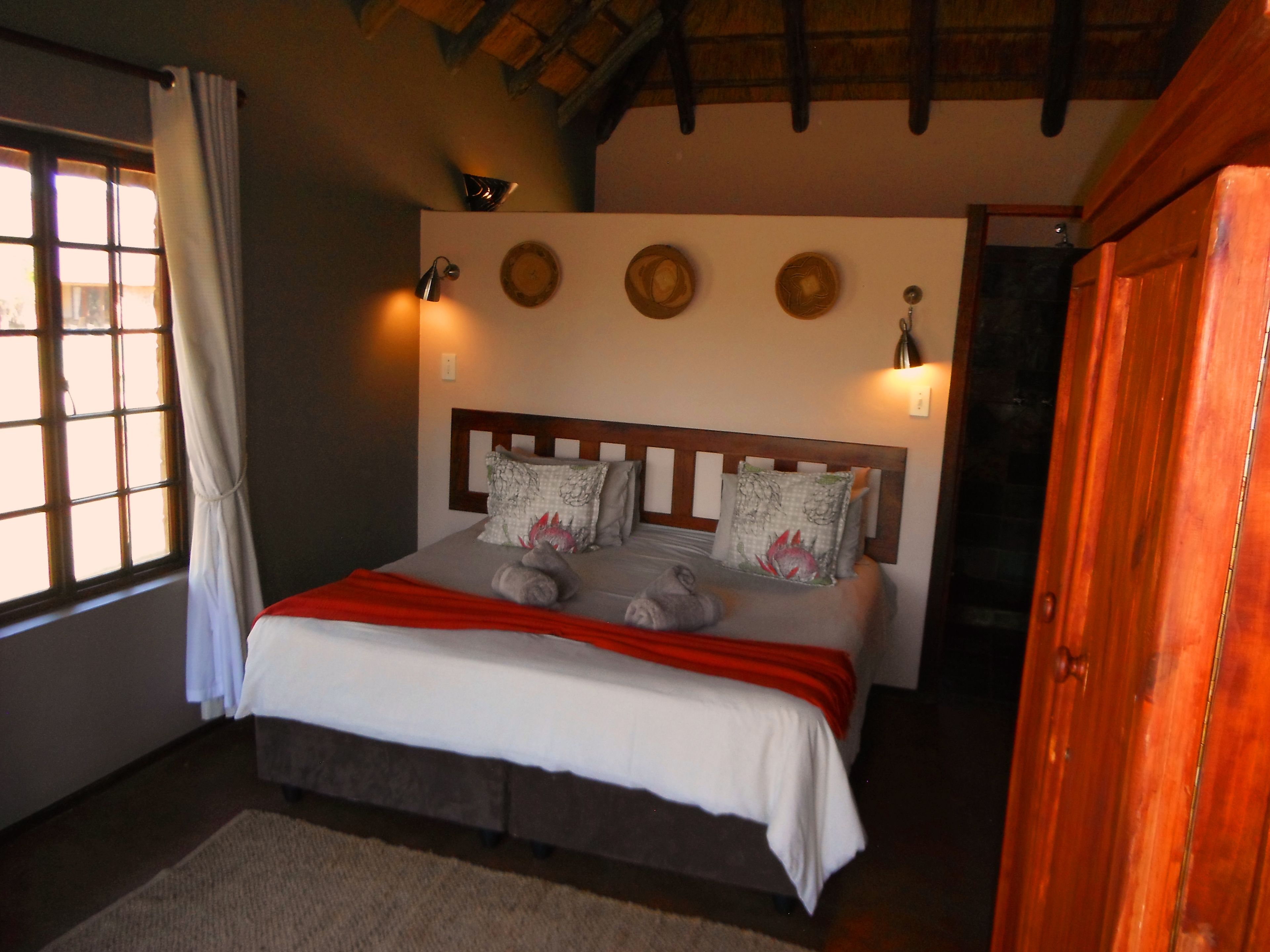 Un dormitorio con cabecera de madera, cama con ropa blanca, almohadas decorativas e iluminación en la pared.