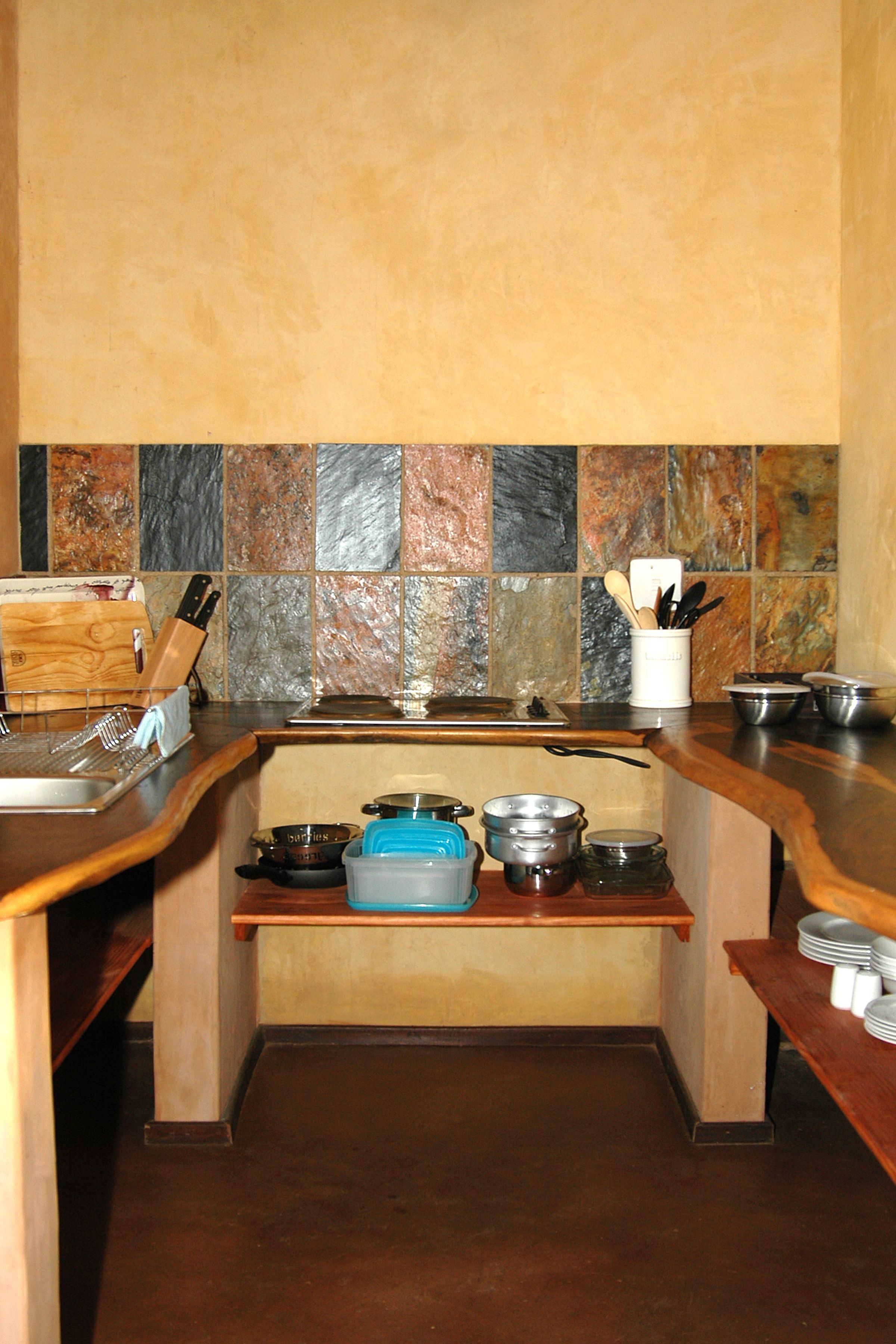 A kitchen with a wooden countertop, a sink, and a backsplash with variously colored tiles.