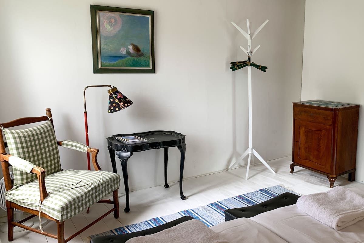 Una habitación con un sillón a cuadros, una pequeña mesa negra, una lámpara de pie alta, un armario y un cuadro en la pared.