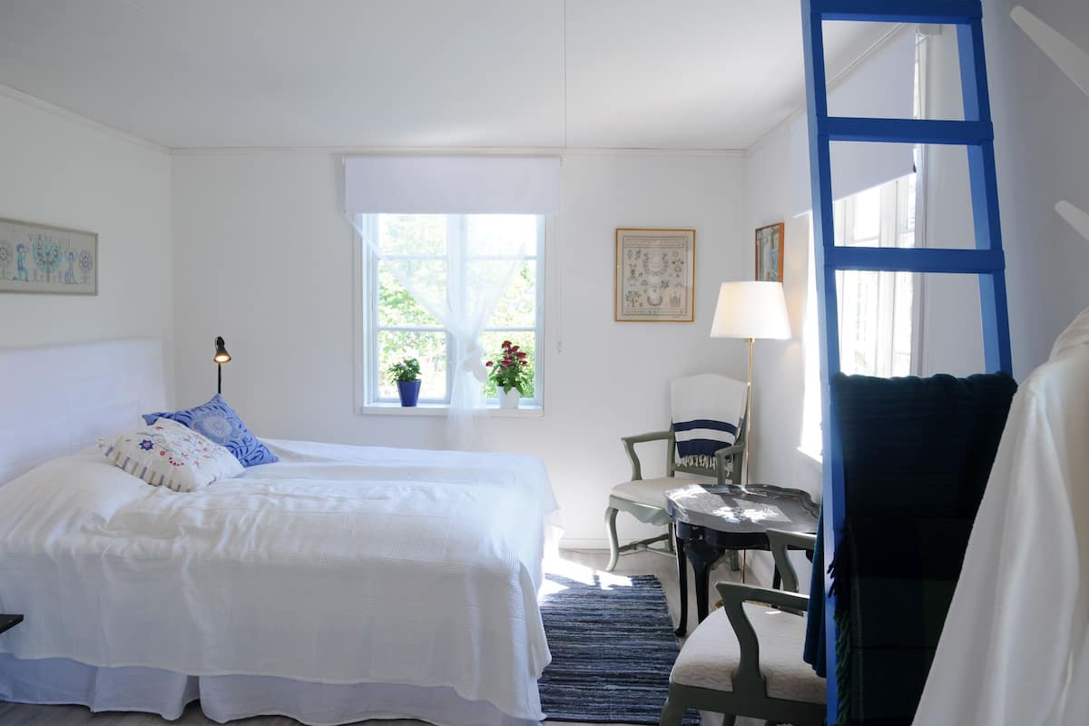 Un dormitorio con cama, escritorio, silla, ventana con plantas y una escalera azul.