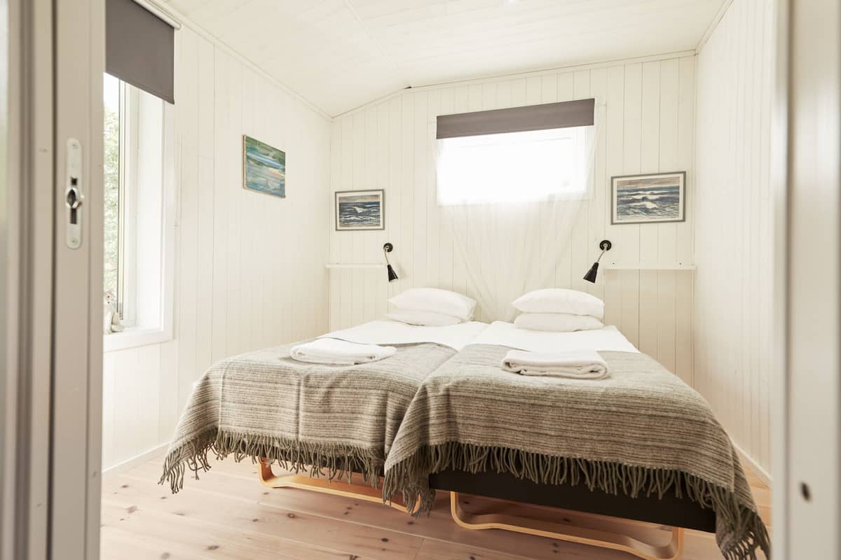Una habitación con dos camas, suelo de madera, paredes blancas y una ventana con vistas.
