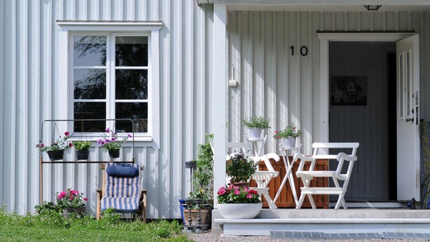 A white building with a number 10 on the door, a window, and a porch with chairs and potted plants. - Villa Weidling B&B (Fengersfors)