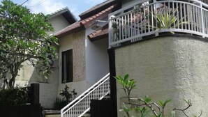 Ein Wohnhaus mit weißer Fassade, einem Balkon mit Geländer und einer Treppe, die zum Eingang führt.