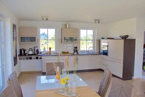 A modern kitchen with a dining table, chairs, and a vase with flowers.