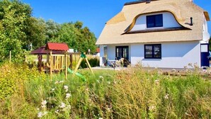 A house with a unique curved roof, a small adjacent structure, and a garden in the foreground. - Tobias house rental - Tobias house (Karlshagen)