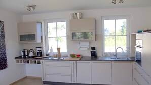 A modern kitchen with white cabinets, a microwave, a coffee maker, and a large window providing natural light. - Tobias house rental - Tobias house (Karlshagen)
