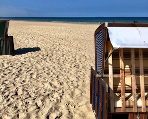 Une plage avec une chaise longue en bois et une chaise en métal à motifs à carreaux.
