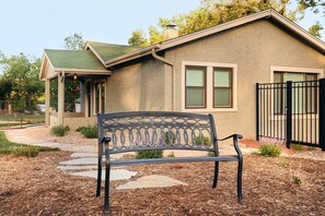 Stucco house with a green roof, featuring two windows with shutters and a black metal gate.
