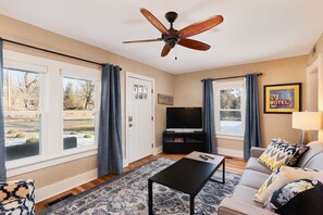 Relax in this inviting living room with a sofa, flat-screen TV, and large windows offering views of the outdoors.
