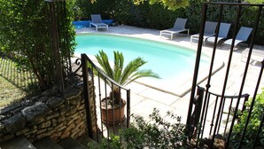 Une piscine entourée de chaises longues, de murs en pierre et de plantes en pot.