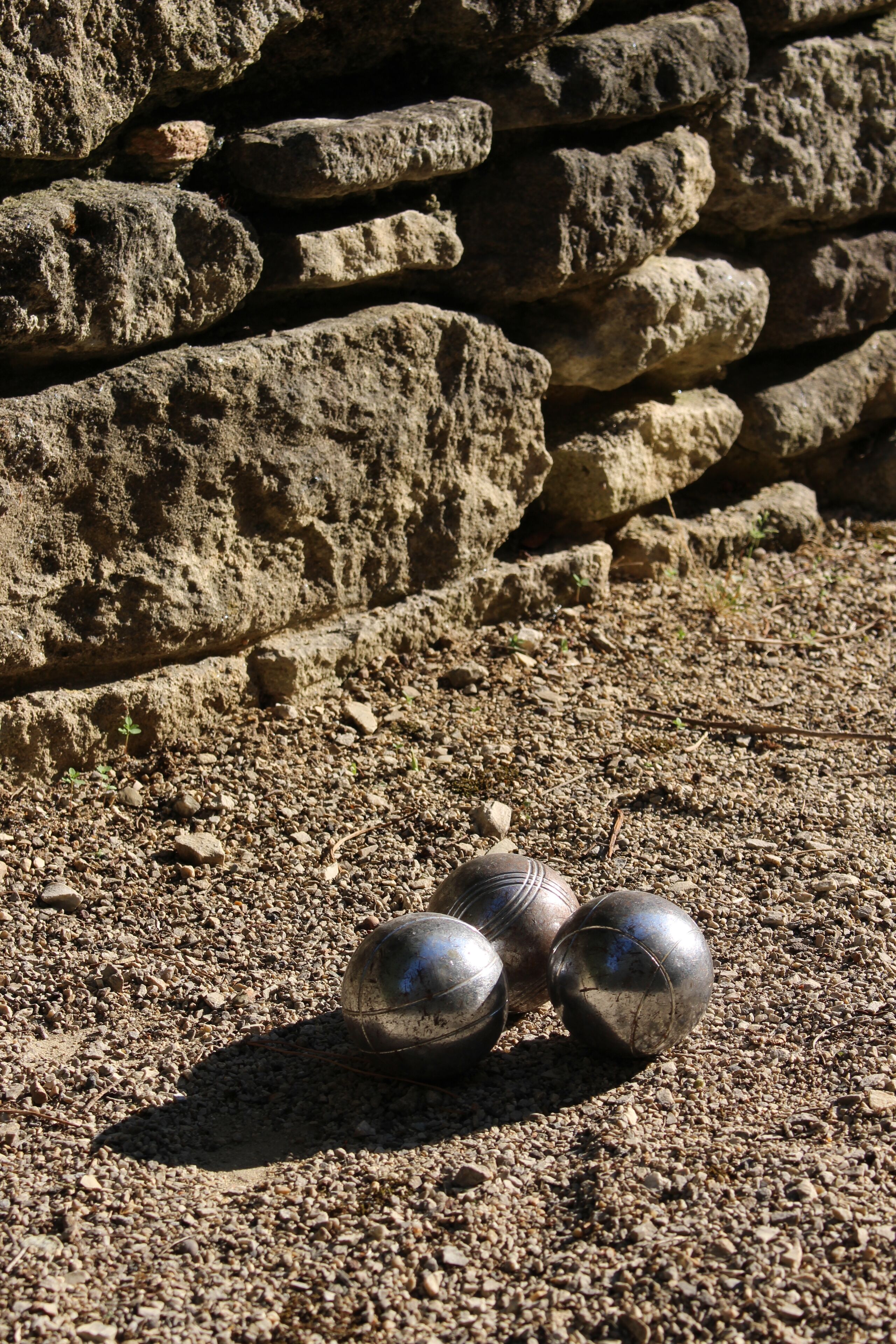 Drei metallische Kugeln auf einer Schotterfläche mit einer Steinmauer im Hintergrund.