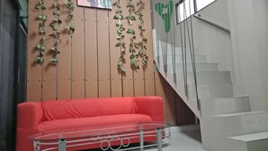 A red sofa, a glass table, and a staircase with a green heart decoration. - Bogor Cabin Inn - Hostel (Bogor)