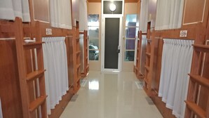 A hallway with wooden shelving units and white curtains, leading to a door with a frosted glass panel. - Bogor Cabin Inn - Hostel (Bogor)