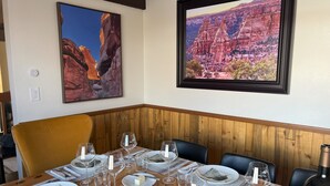 A dining area with a wooden table set for a meal, two framed landscape paintings on the wall, and a yellow chair. - Views+, Spacious Home, Hot Tub, Ski/Hike/Golf, base of the CO Nat'l Monument! (Grand Junction)