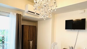 A bedroom with a large bed, a chandelier, a TV mounted on the wall, and a small table with chairs. - Davao Boutique Condos - Near Abreeza (Davao)