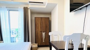 A hotel room with a bed, a dining table with chairs, a chandelier, an air conditioning unit, and a television mounted on the wall. - Davao Boutique Condos - Near Abreeza (Davao)