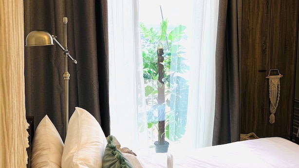 A hotel room with a bed, pillows, a bedside lamp, a window with curtains, and a view of greenery outside. - Davao Boutique Condos - Near Abreeza (Davao)