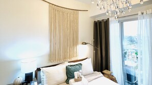 A hotel room with a large bed, a chandelier, a bedside table with a lamp, and a view of the outside through the window. - Davao Boutique Condos - Near Abreeza (Davao)