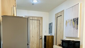 A modern kitchen with a white bench, wooden cabinets, and a microwave on a white cabinet. - Davao Boutique Condos - Near Abreeza (Davao)